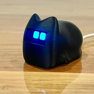 Black loaf-shaped cat desk robot with glowing blue eyes on a wooden table