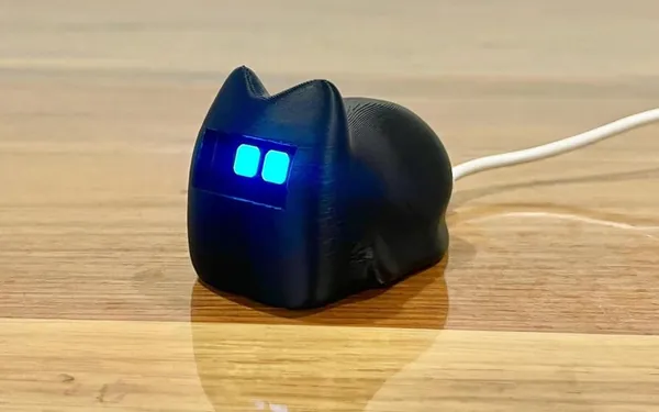 Black loaf-shaped cat desk robot with glowing blue eyes on a wooden table