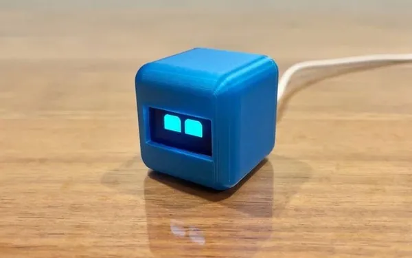 Small blue cube robot with glowing eyes on a wooden table